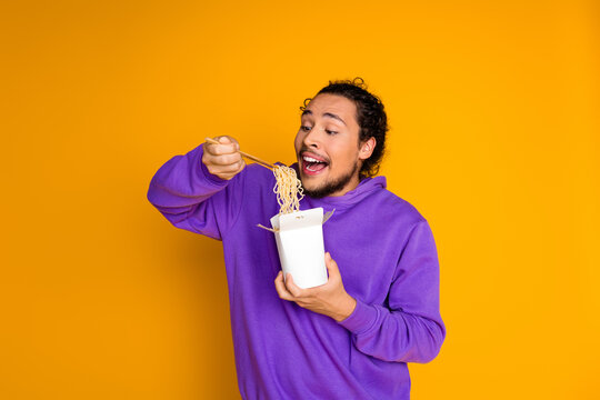 Young man enjoying takeaway noodles with chopsticks on yellow background in casual style - Powered by Adobe