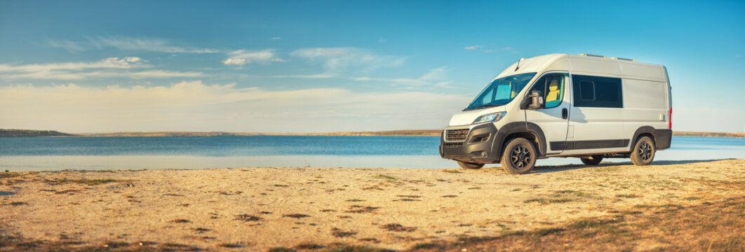 Panoramic view to sea coast with white camper van on wild beach with copy space