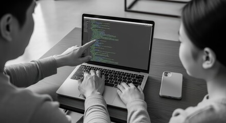Two people collaborating on programming code at laptop indoors