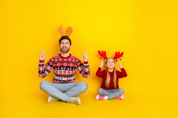 Father and daughter celebrating Christmas in festive attire with joyful expressions against a vibrant yellow background
