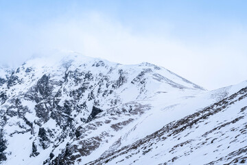 Fototapeta premium Snow-Capped Mountain Peaks Hidden in Misty Fog