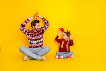 Father and daughter wearing Christmas antlers and sweaters playfully posing against a vibrant yellow background