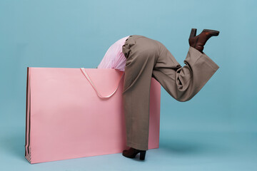 Funny shopper diving into giant pink shopping bag on blue studio background