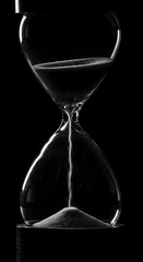 Time's Precious Flow: A monochromatic hourglass captures the silent passage of time, a delicate dance of sand grains elegantly cascading from top to bottom against a dark backdrop.