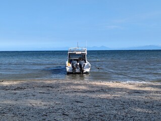 Boat on calm sea shore with beach under sunny blue sky. Ideal for travel brochures, vacation websites, seaside advertisements.
