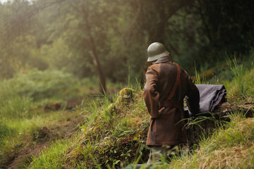 Soldier in vintage uniform standing near bunker in forest during wartime scene.