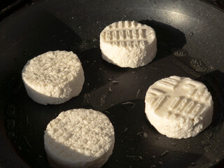 Four round pieces of goat cheese heating in a black non stick pan, preparing for a warm salad or quick appetizer, enjoying the cooking process