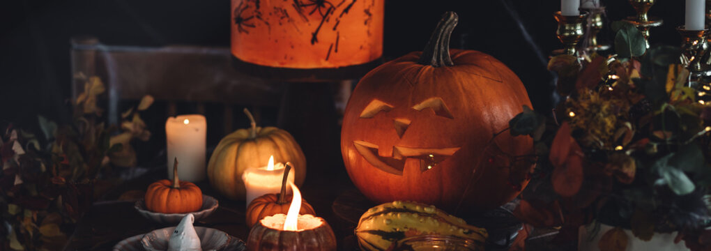 Beautiful table with homemade delicious cake for Halloween party with meringue ghosts and chocolate pumpkins. Candles in chandelier, spider web, jack-o-lantern for festive holiday decoration. Banner