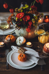 Beautiful elegant table setting for candlelight Thanksgiving Day dinner or Halloween party at home. Fancy dishware, porcelain plates. Floral centrepiece, pumpkins and burning candles as decor