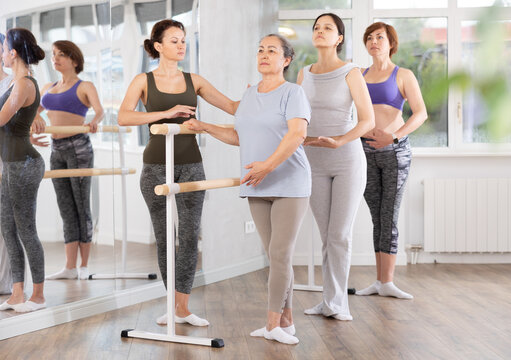Adult female teacher corrects movements of novice dancers in studio