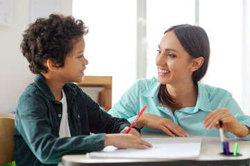 Obraz premium Happy female teacher helping Latin boy with task in secondary school during test. Support, scholarship and educator aid