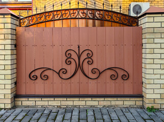 A wooden fence with iron elements between brick pillars. Fencing design concept for urban architecture and landscapes.