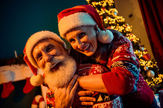 Joyful elderly couple hug Santa in a cozy home Christmas scene with a decorated tree and warm lights - Powered by Adobe
