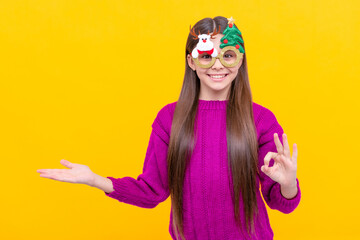 happy kid in party glasses presenting product on yellow background, new year