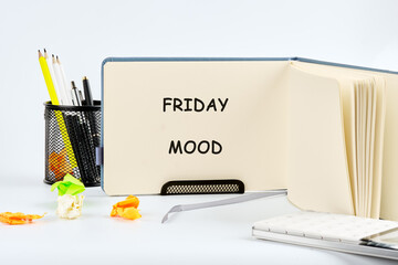 A notepad reads FRIDAY MOOD on a work desk. Crumpled papers suggest a long week. Office supplies and a notebook complete this relatable lifestyle scene