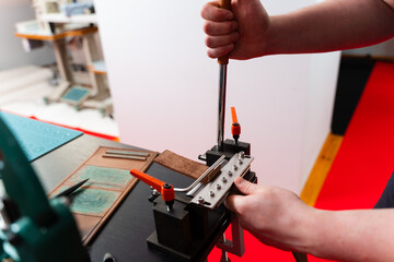 Craftsman shapes a leather strap with an edge creasing machine. Leatherworker uses a creasing press...