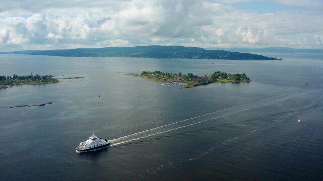 Drone footage of Ferry cruising through Oslofjord in Norway, surrounded by green islands and calm summer waters. Scenic Scandinavian landscape of coastal Oslo capital city. 4K wide shot