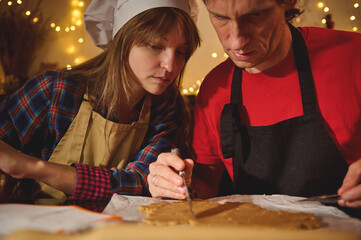Holiday Kitchen Duo: Woman In Chef Hat And Apron Shapes Dough While Man In Red Shirt And Black Apron Guides Cutter During Festive Baking