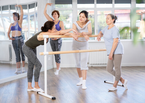 Group of women of various ages, passionate about ballet, friendly chatting while relaxing at barre after amateur rehearsal in well-lit dance studio - Powered by Adobe
