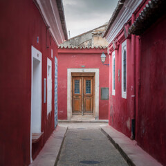 View of vibrant red walls embracing a narrow cobblestone street, adorned with potted plants and vintage lanterns, creating a captivating scene, Arequipa, Peru.