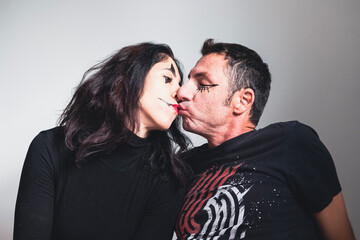 Husband and wife with face makeup for Halloween kiss on light background. The man and woman are thirty-eight years old and of Caucasian origin