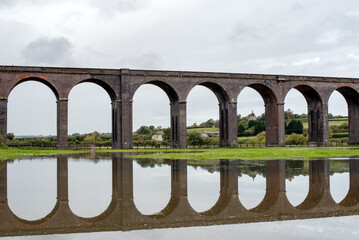 Large railway viaduct with multiple arches reflected in water near Harringworth, England.