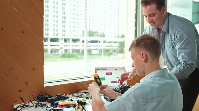 Caucasian teacher help student fixing car model and giving advise for programming system or coding prompt while high school boy listen and use equipment to repair robot at STEM classroom. Edification