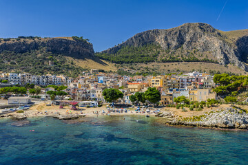 Fototapeta premium Sant Elia bay beach in Porticello town, Santa Flavia, Sicily, Italy, aerial drone view of Sicilian turquoise waters, rocky cliffs, colorful houses, and Mediterranean coastline panorama in Bagheria