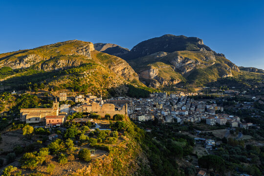 Aerial drone view of Collesano Sicilian mountain town at sunset with Basilica San Pietro church and historic stone streets in the Madonie Mountains, Sicily, Italy. Old mountain town in Sicily
