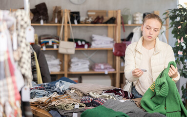 Attentive teen girl looking for warm pullower while shopping in retail outlet