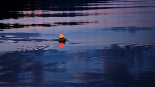 Fishing float gently bobbing in the calm evening lake creating soft ripples at dusk