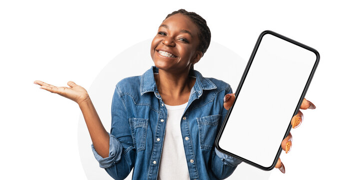 A cheerful woman is happily displaying a blank smartphone in her hand. She is wearing a denim jacket and looks excited. The background is simple and bright, enhancing her joyful expression.