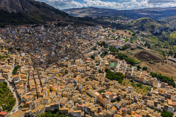 Aerial drone view of Caltavuturo, a historic Sicilian mountain town in Palermo, Italy, featuring its medieval castle, rugged surrounding cliffs, and scenic landscapes of the Madonie Mountains