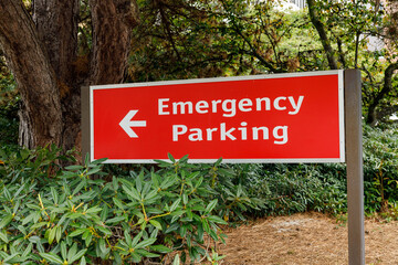 Fototapeta premium Red emergency parking sign with left arrow, nestled in lush green shrubs and tall trees on a serene woodland path