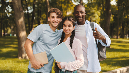 Happy students. Portrait of joyful university friends embracing and posing together outdoors in campus or park, holding workbooks and smiling at camera