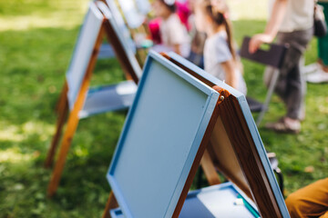Kids drawing at plein air, group class of talented children with painting easel and wooden canvas...