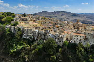 Naklejka premium Aerial drone view of Polizzi Generosa, a picturesque Sicilian mountain town perched on rocky cliffs showcasing traditional stone buildings and panoramic views of the Madonie Mountains, Sicily, Italy