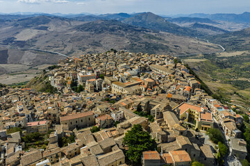 Fototapeta premium Aerial drone view of Polizzi Generosa, a picturesque Sicilian mountain town perched on rocky cliffs showcasing traditional stone buildings and panoramic views of the Madonie Mountains, Sicily, Italy