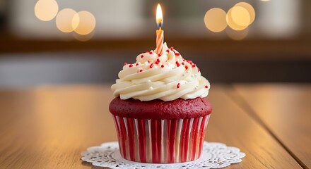 Delicious red velvet cupcake with lit candle on table with celebration and bokeh background.