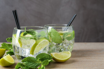 Glasses of tasty cocktails with lime and mint on wooden table, closeup. Space for text