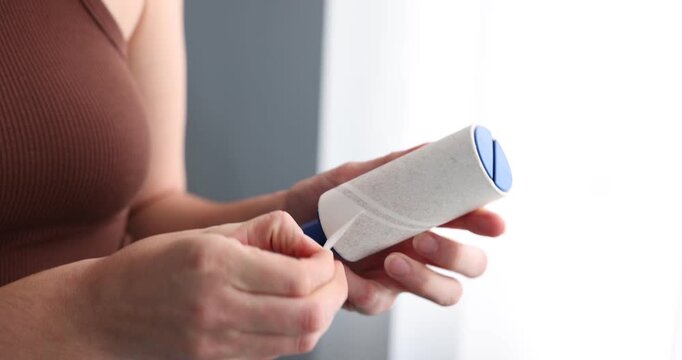 Woman removing sticky tape from lint roller indoors, closeup