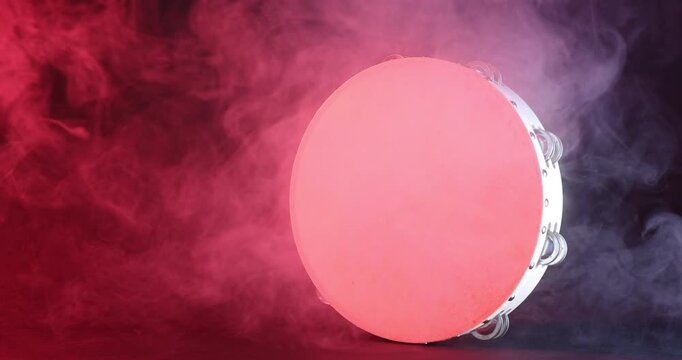 Tambourine in color light on dark background with smoke