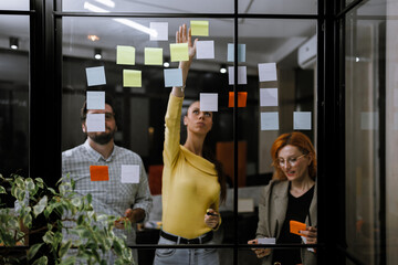 Team collaboration during brainstorming session in modern office with sticky notes on glass wall
