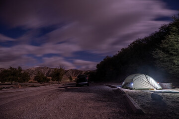 Tent camping with bright lights under the cloudy blue sky as stars begin to emerge over the canyon