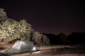 Illuminated tent camping under the clear dark sky as the last light of the day fades behind the canyon and the stars shine bright