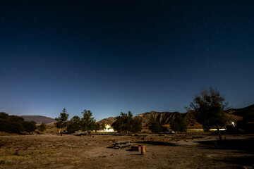 Camping under the clear night sky full of stars as the sun sets behind the canyon peaks