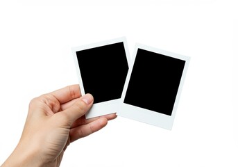Hand holding two blank instant photo frames against a white background.