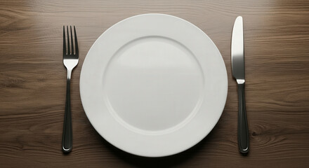Empty white plate with cutlery on wooden table.