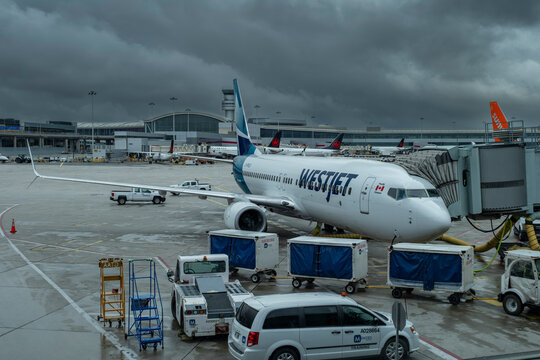 Westjet airplane, airport equipment and infrastructure with dark rainstorm clouds in background at Toronto Pearson Airport (GTAA). Transportation, air travel and tourism industry concept.