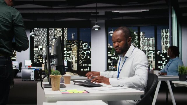 Black young employee proofreading financial data for a new report at night, reviewing archived files in the strategy room. Evaluating data, researching and organizing agenda. Camera A.